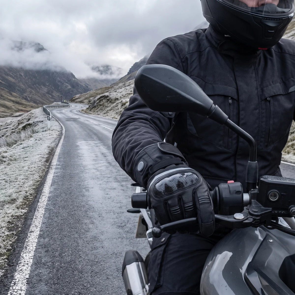 Motorradfahrer auf einer kalten Passstraße, Hände in beheizten Handschuhen am Lenker