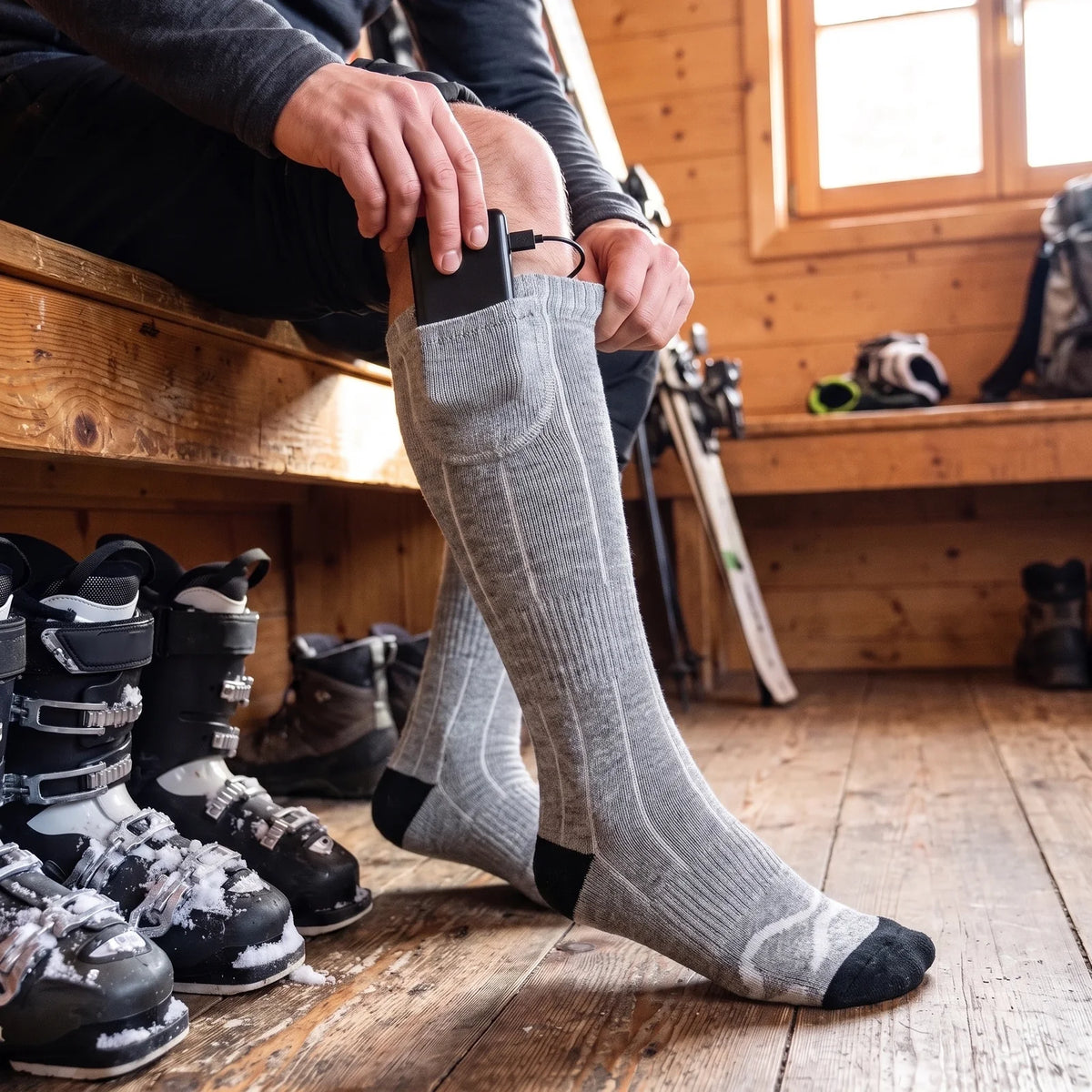 Akku wird in die Tasche am Bund des beheizten Kniestrumpfs gesteckt, Skischuhe in der Hütte
