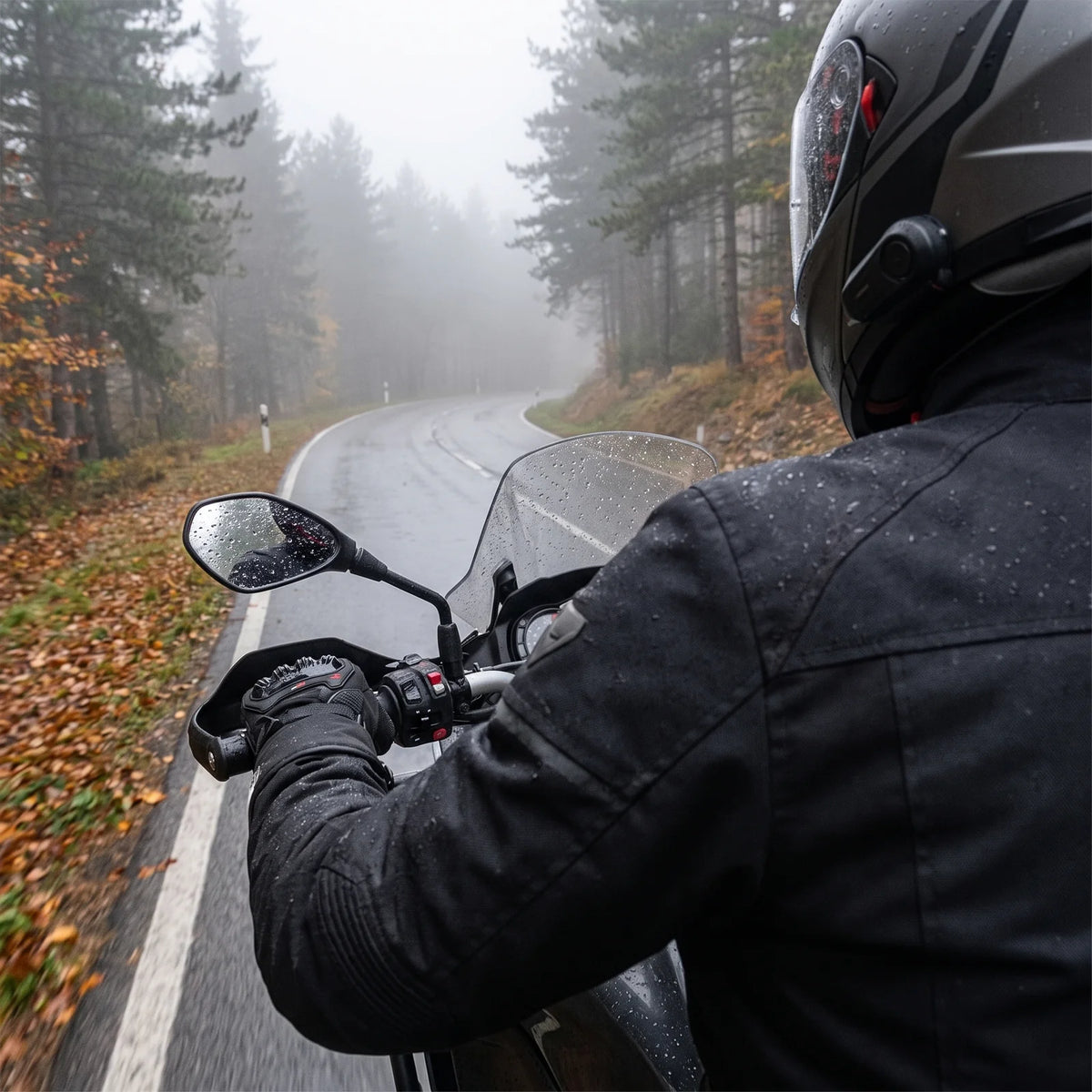 Motorradfahrer mit Winterhandschuhen am Lenker auf nasser Bergstraße im Nebel